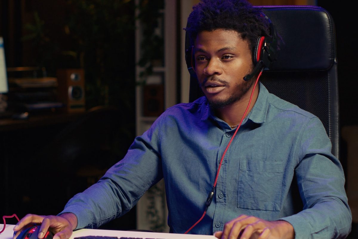 Man playing intense game on rgb lit computer desktop, talking with fans during livestream. African american gamer in neon lit room focused on esports online videogame on PC